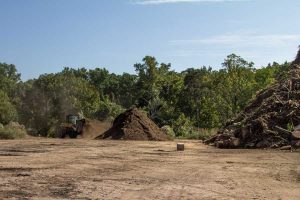 Two mounds of different material accompanied by a dump truck and trees in background
